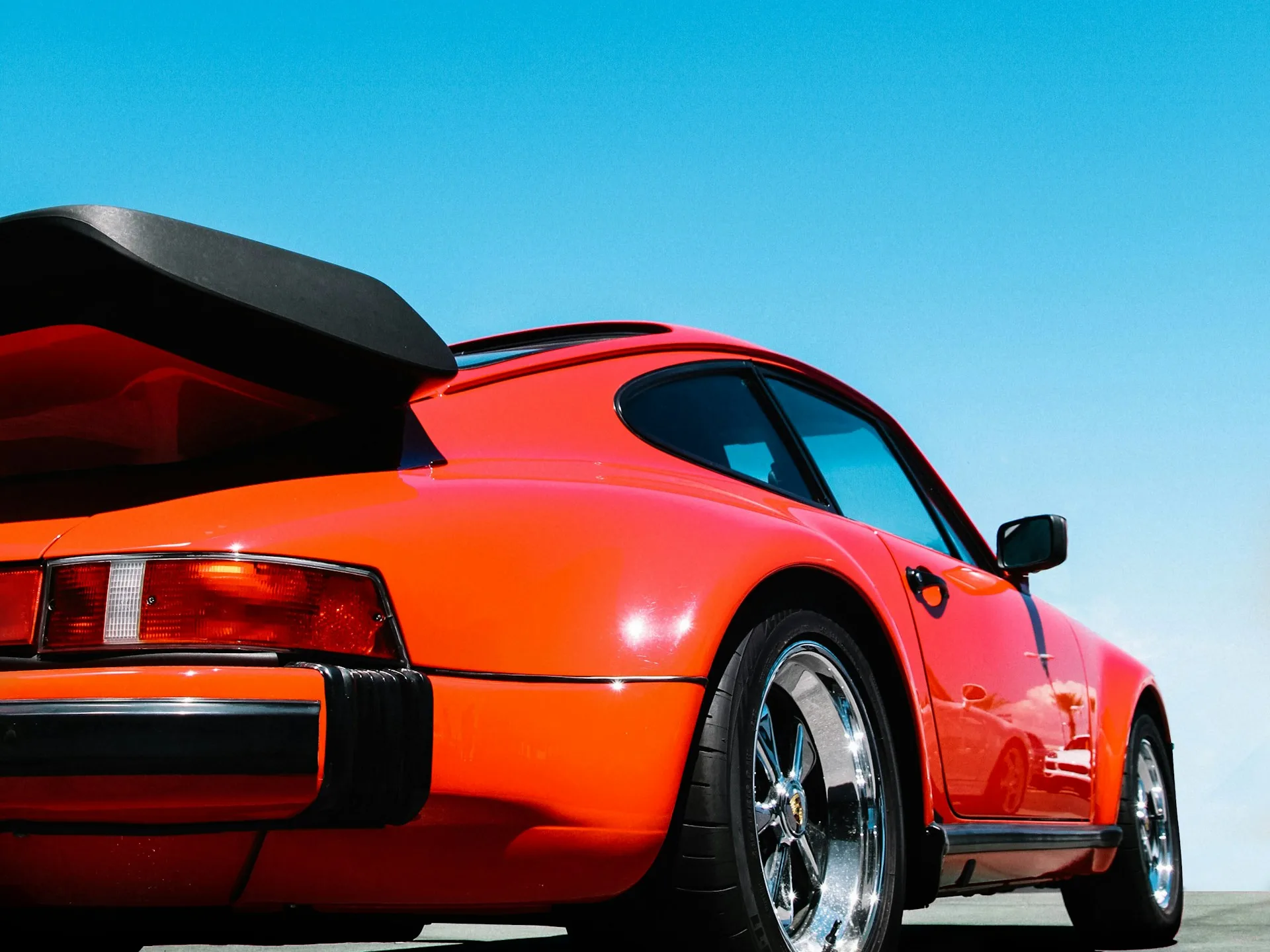Porsche 911 orange vue de trois quarts arrière sous un ciel bleu